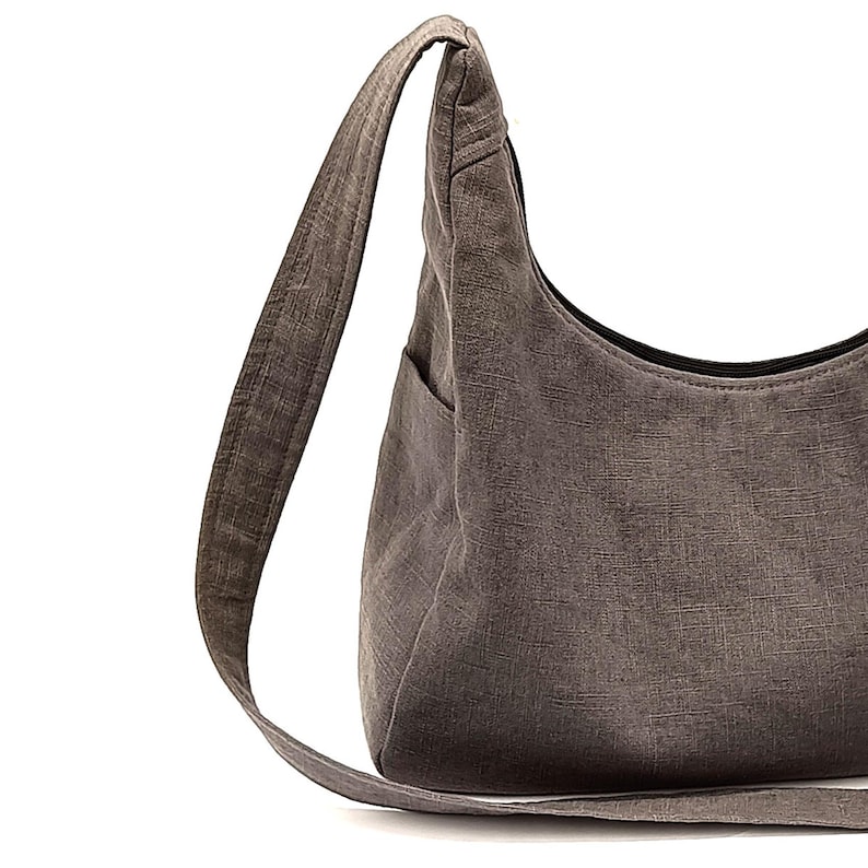 May include: A grey canvas shoulder bag with a long strap. The bag has a single pocket on the front.