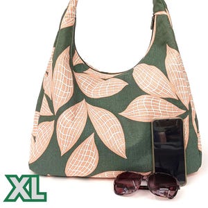 May include: A large green and peach-coloured tote bag with a zip closure and a leaf pattern. The bag is labelled "XL" and has a mobile phone and sunglasses resting on top of it.