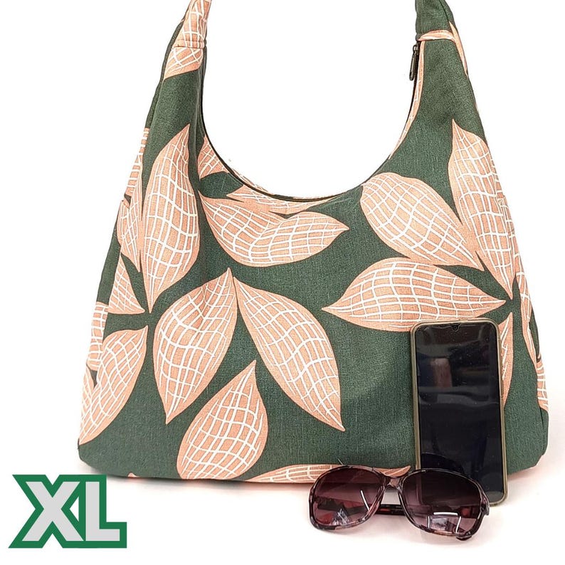 May include: A large green and peach-coloured tote bag with a zip closure and a leaf pattern. The bag is labelled "XL" and has a mobile phone and sunglasses resting on top of it.