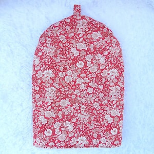 May include: A dome-shaped fabric tea cozy featuring a vibrant red background with a dense, repeating white floral pattern of various small blossoms and leaves, finished with a small fabric loop at the top center for easy handling and storage.