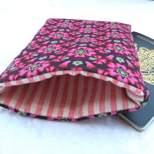 May include: A floral passport cover with a pink and black flower pattern on the exterior. The interior lining features red and white stripes. A British passport is visible in the background.