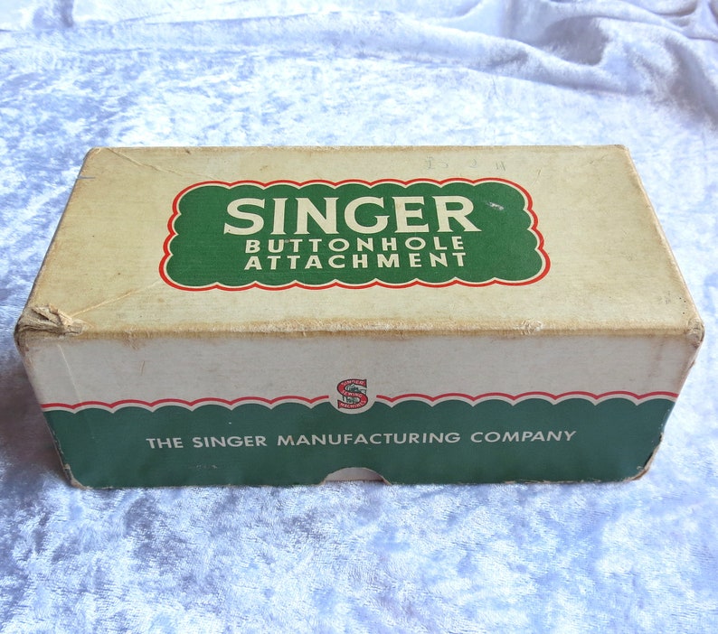 May include: A vintage Singer buttonhole attachment box with green and red accents. The box is labeled "Singer Buttonhole Attachment" and "The Singer Manufacturing Company".