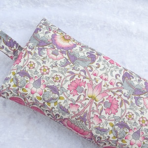 May include: A white fabric doorstop with a floral pattern in shades of pink, purple, and grey. The doorstop has a loop handle.