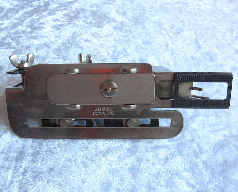 May include: A silver metal sewing machine foot with a black plastic piece and the text "86662 COMPLETE" on the side.