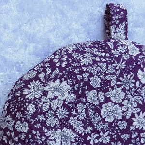 May include: Purple fabric pot holder with a white floral pattern and a loop handle.