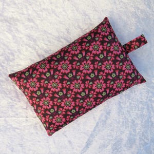 May include: Rectangular pillow with a floral pattern in shades of pink, green, and brown. The pillow has a small fabric loop attached to one end. The floral design is repeated across the surface of the pillow.