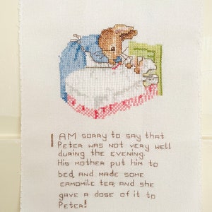 Könnte beinhalten: Eine Kreuzstich-Stickerei von Peter Rabbit im Bett mit einer Tasse Tee. Der Text lautet: "AM SORRY to SAY that PETER WAS NOT VERY well during the EVENING. HIS MOTHER Put him to BED, AND MADE SOME CAMOMILE TER; And she GAVE A dose of it to PETER."
