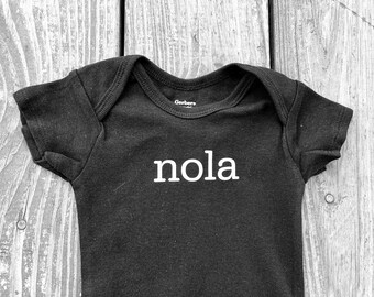 May include: Black baby onesie with white text that says "nola" on the front.