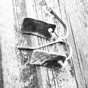 May include: A pair of silver earrings with a hammered rectangular shape. The earrings have a simple wire hook closure.