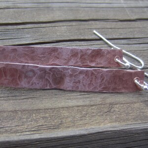 May include: A pair of hammered copper earrings with silver hooks. The earrings are a light pink color and have a textured surface.