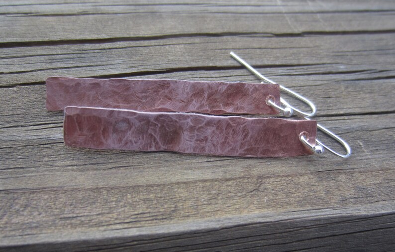 May include: A pair of hammered copper earrings with silver hooks. The earrings are a light pink color and have a textured surface.