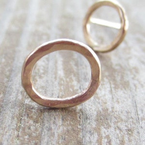 May include: A pair of gold-toned circle stud earrings. The earrings are made of a hammered metal and have a simple, minimalist design.