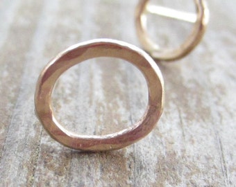May include: A pair of gold-toned circle stud earrings. The earrings are made of a hammered metal and have a simple, minimalist design.