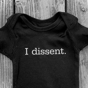 May include: Black baby onesie with the text "I dissent." printed in white.