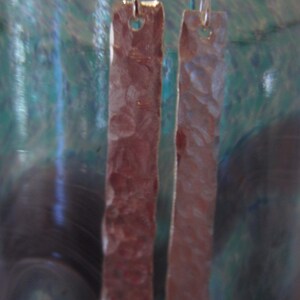 May include: A pair of silver earrings with a hammered texture. The earrings are rectangular in shape and hang from silver hooks.