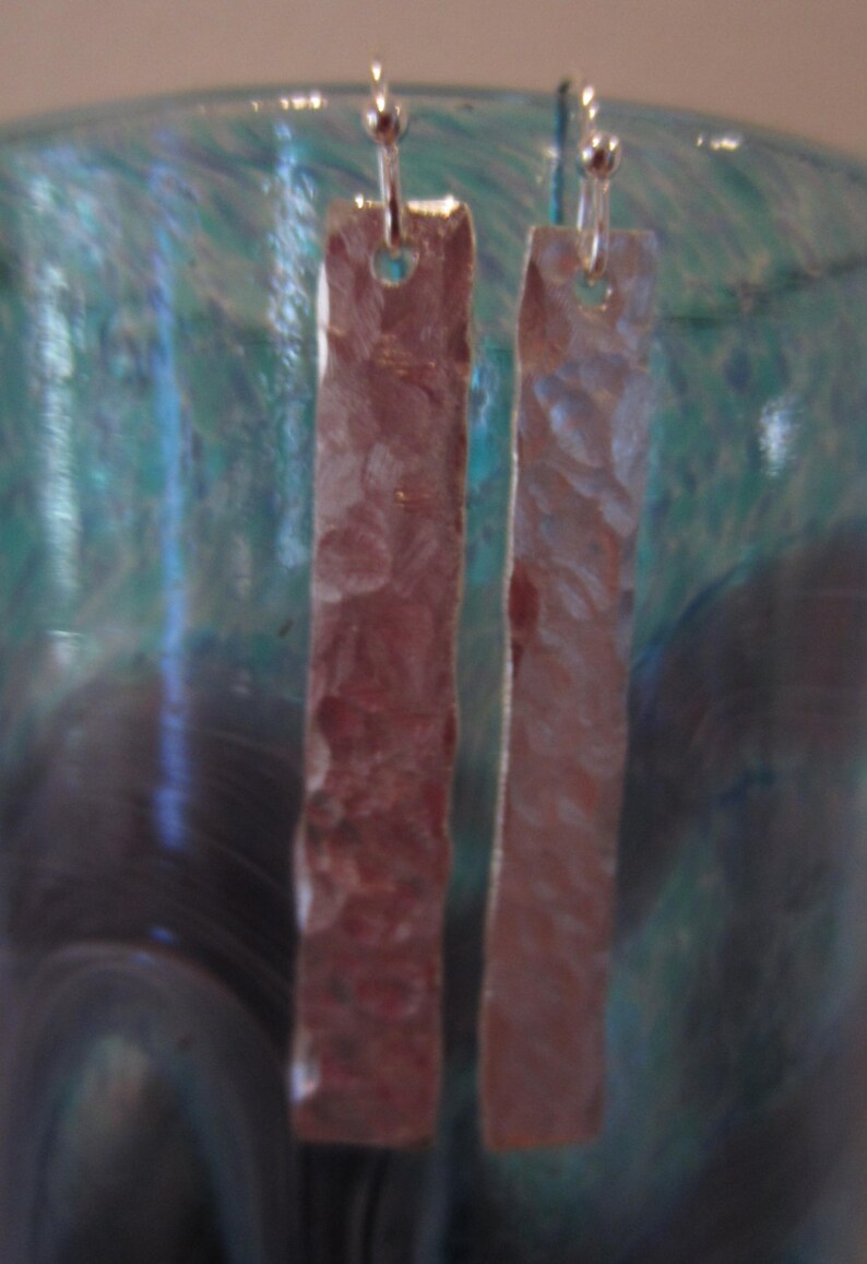 May include: A pair of silver earrings with a hammered texture. The earrings are rectangular in shape and hang from silver hooks.