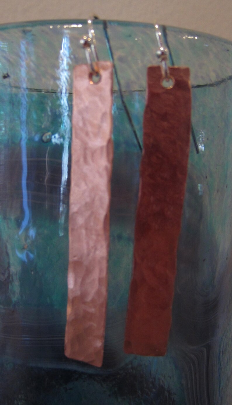 May include: A pair of hammered copper earrings, one is a light pink color and the other is a reddish brown color.
