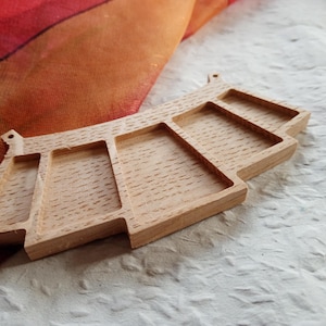 Op de afbeelding: Een lichtgekleurde houten serveerschaal met meerdere compartimenten. De schaal heeft een uniek architectonisch ontwerp met rechthoekige en trapeziumvormige secties. De houtnerf is zichtbaar en de schaal ligt op een getextureerd wit oppervlak.