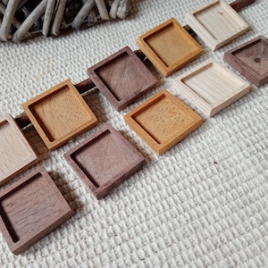 Puede incluir: Surtido de nueve bandejas de exhibición cuadradas de madera en varios tonos de marrón, marrón claro y madera natural. Las bandejas están dispuestas en una fila sobre una superficie texturizada.