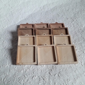 以下が含まれることがあります： 12個の未完成の正方形の木製ペンダントトレイのセット。トレイは4つずつ3列に配置されており、一番上の列は最も濃い木の色、一番下の列は最も薄い木の色になっています。