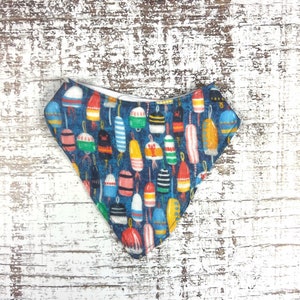 May include: A blue bandana with a white border and a pattern of colorful buoys.
