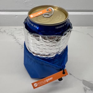 Puede incluir: Un enfriador de latas azul con una capa aislante plateada y una bolsa de cordón azul. El enfriador de latas tiene el texto "minusgear" y "Founded in the USA" impreso en él. La bolsa de cordón tiene el texto "minusgear" y "Unmistakable Style" impreso en ella.
