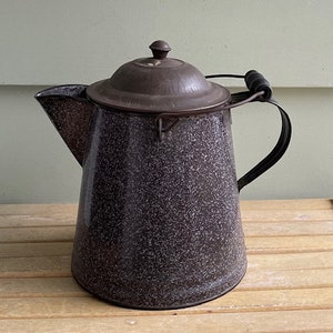 May include: A vintage gray speckled enamel coffee pot with a black metal handle and a lid. The pot has a rustic look and is perfect for serving coffee or tea.