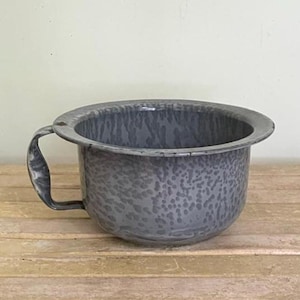 May include: A gray enamel basin with a speckled pattern and a single curved handle on the side. The bowl features a wide, flat rim and a deep, rounded body, showcasing a consistent mottled gray finish throughout the entire exterior surface.