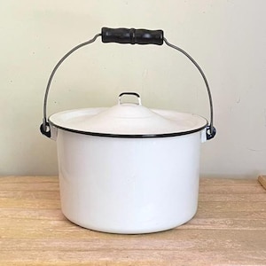 May include: A white enamel pot with a matching lid and a black rim. The pot features a metal swing handle with a black wooden grip. The cylindrical container has a smooth finish and a simple design, providing a functional vessel for storage or cooking.