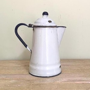 May include: A white enamel coffee pot with a dark blue handle, a matching dark blue lid knob, and a dark blue rim. The pot features a tapered body, a side spout, and visible signs of wear including small chips in the enamel coating.