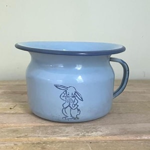 May include: A light blue enamel chamber pot featuring a dark blue rim and a matching handle. The front of the vessel is decorated with a dark blue line drawing of a rabbit standing upright with its ears positioned back.