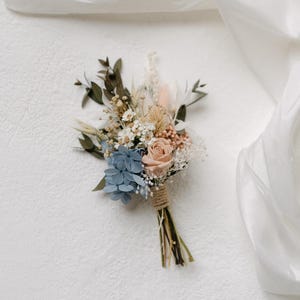 May include: A small bouquet of dried flowers tied with twine. The bouquet includes blue hydrangeas, a peach-colored rose, and white baby's breath.