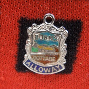 May include: Silver charm with a blue, green, and yellow enamel design. The charm features the text "Burns Cottage Alloway".