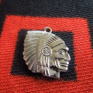 May include: Silver charm pendant featuring a profile of a Native American man wearing a feathered headdress. The charm is detailed with a beaded design and a small circular symbol on the headdress.