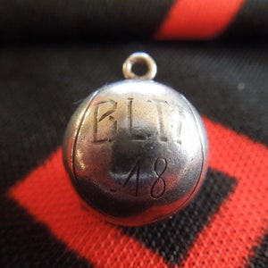 May include: A silver charm in the shape of a ball with the letters "BLT" and the number "48" engraved on it.