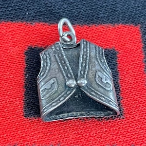 May include: A silver charm in the shape of a vest with intricate details and two small round buttons.