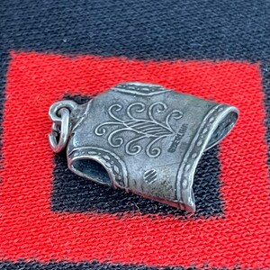 May include: Silver charm in the shape of a suit of armor with a decorative design. The charm has a loop for attaching to a bracelet or necklace. The charm is marked "Sterling".