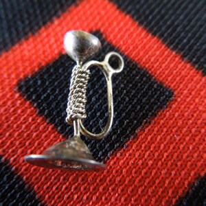 May include: A silver charm in the shape of a trumpet. The charm is detailed with a coiled design and a loop for attaching to a bracelet or necklace.