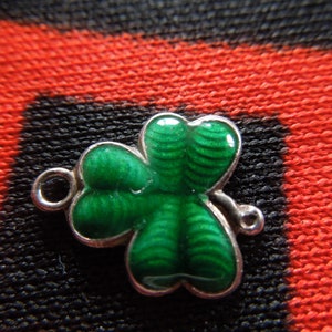 Puede incluir: Un amuleto de plata en forma de tr&eacute;bol verde con un bucle para sujetarlo a una pulsera o collar.