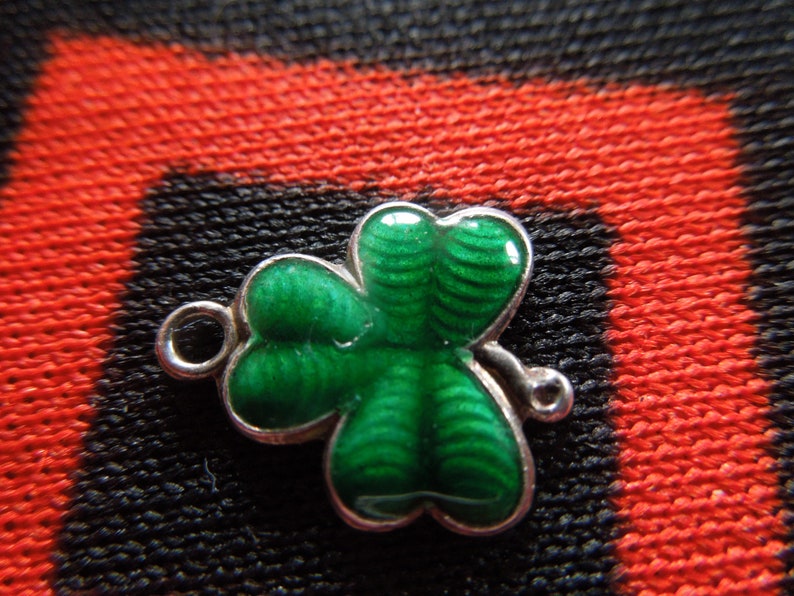 Puede incluir: Un amuleto de plata en forma de tr&eacute;bol verde con un bucle para sujetarlo a una pulsera o collar.
