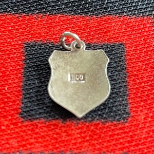 May include: Silver charm in the shape of a shield with the year 1900 stamped on the back.