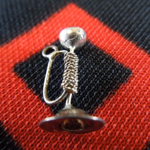 May include: Silver charm in the shape of a hookah, a traditional water pipe. The charm has a round top and a long, thin stem.