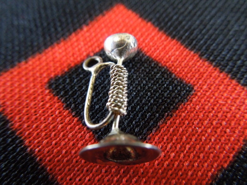 May include: Silver charm in the shape of a hookah, a traditional water pipe. The charm has a round top and a long, thin stem.