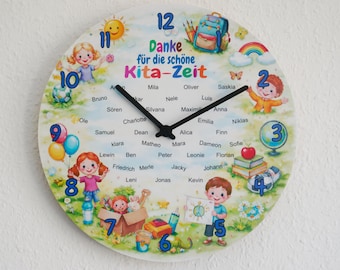 May include: A round wall clock featuring a colorful illustration of children, a backpack, a rainbow, and school supplies. The clock face displays the German text Danke für die schöne Kita-Zeit and a list of names, with blue numbers and black hands.