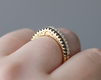 Può includere: Un anello d'oro con un designo di pietre nere e bianche. L'anello è indossato su un dito.