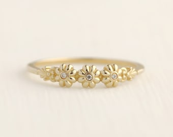 May include: A gold ring with three small, detailed flower designs, each with a single diamond in the center.