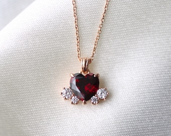 May include: A rose gold necklace with a heart-shaped red gemstone pendant surrounded by smaller clear gemstones.