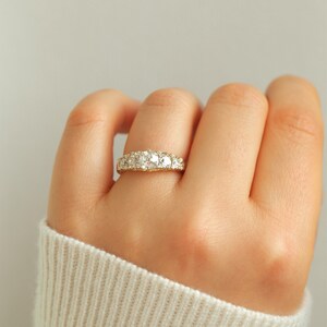 May include: A gold band ring with a row of round, clear gemstones.
