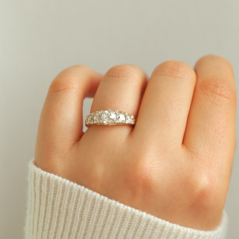 May include: A gold band ring with a row of round, clear gemstones.