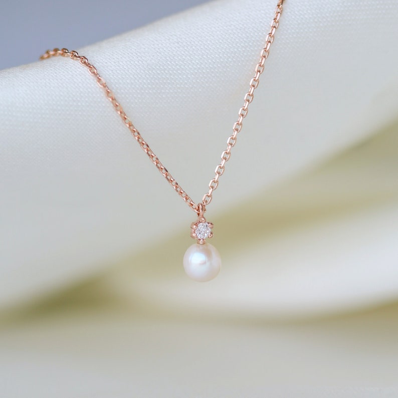 May include: A delicate rose gold necklace with a single pearl pendant and a small diamond accent.